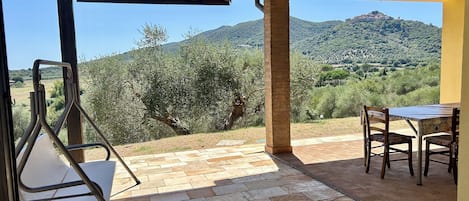 A covered outdoor seating area with a table and chairs, overlooking a mountainous landscape.