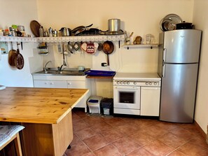 Une cuisine avec une table en bois, des placards blancs, une cuisinière, un évier et un réfrigérateur.
