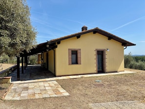 A single-story building with a tiled patio, a covered outdoor seating area, and a view of the surrounding landscape. - Cottage nestled among the olive trees, dogs welcome (Tuscany)