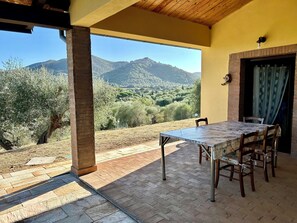 An outdoor patio with a table and chairs, a brick floor, and a view of a mountainous landscape. - Cottage nestled among the olive trees, dogs welcome (Tuscany)