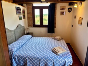 A bedroom with a bed, a nightstand, a window with curtains, and wall decorations. - Cottage nestled among the olive trees, dogs welcome (Tuscany)
