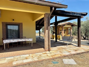 A covered patio area with a table and chairs, a brick wall, and a pergola structure. - Cottage nestled among the olive trees, dogs welcome (Tuscany)
