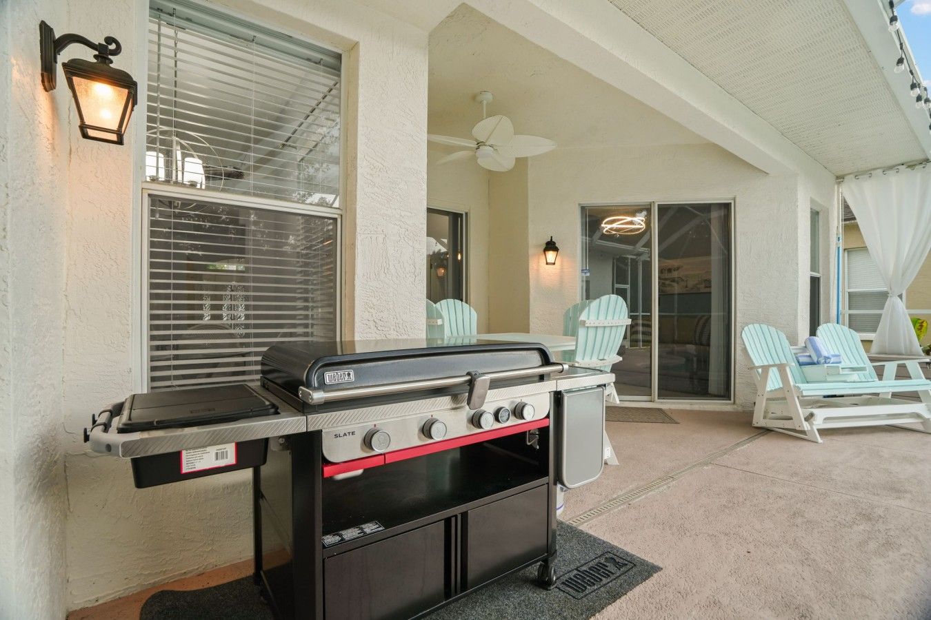 An outdoor patio with a barbecue grill, two Adirondack chairs, and a ceiling fan.