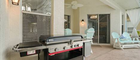 An outdoor patio with a barbecue grill, two Adirondack chairs, and a ceiling fan.