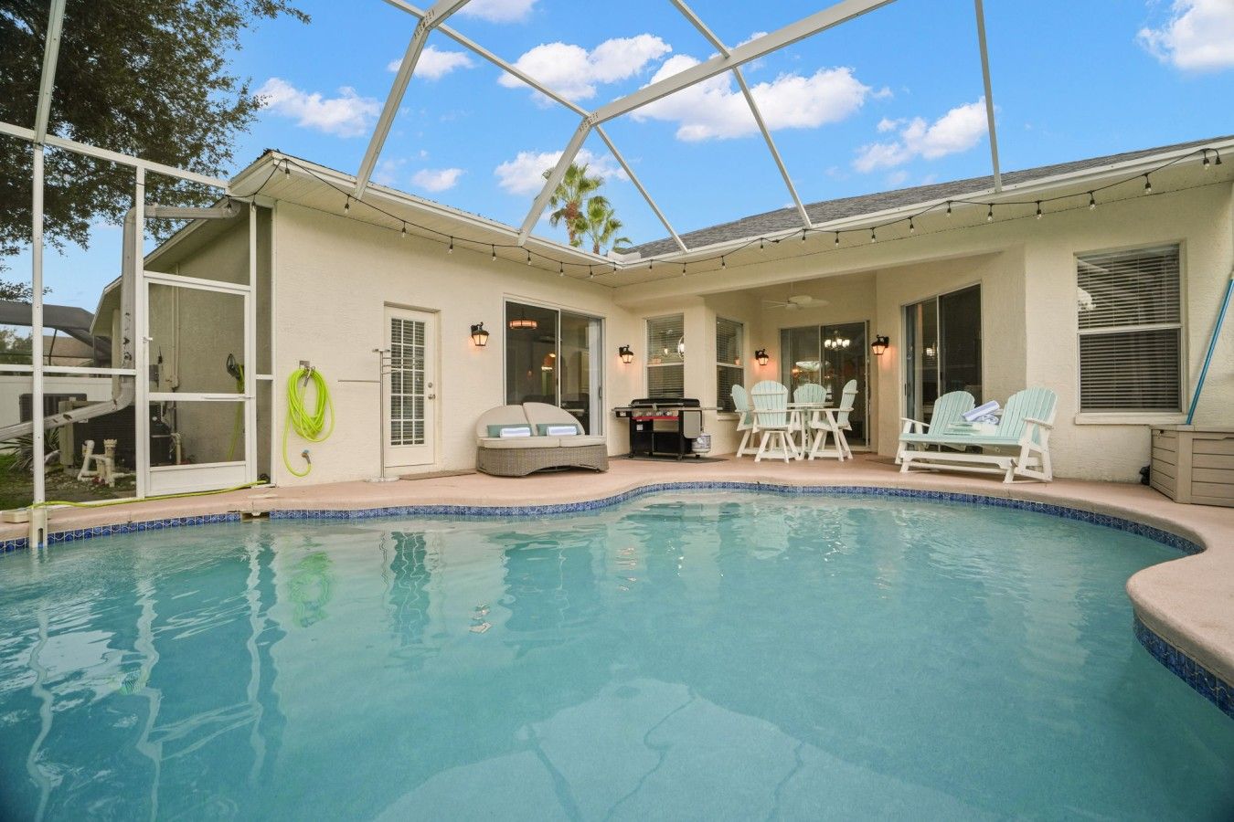 A pool area with a covered patio, outdoor seating, and a grill.