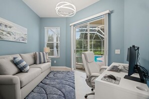 Ein modernes Wohnzimmer mit einer Couch, einem Schreibtisch mit Computer und einem großen Fenster mit Blick auf einen Pool.