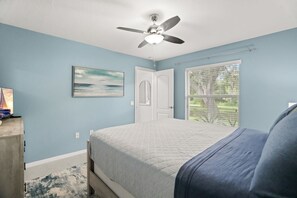 A bedroom with a bed, a ceiling fan, a window with blinds, and a door.