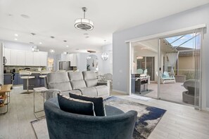 A modern living room with a grey sectional sofa, a dining area, and a kitchen in the background.