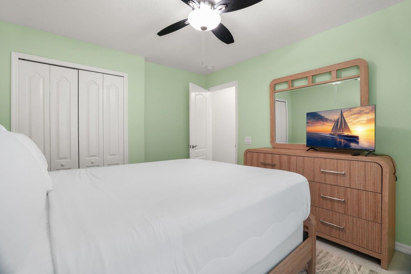 A bedroom with a bed, a dresser, a television, and a ceiling fan.