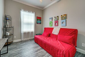 Ein Zimmer mit rotem Sofa, einem Fenster mit Jalousien, einem Regal mit Dekoration und Wandbildern.