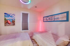 Ein Schlafzimmer mit zwei Betten, einem Fenster mit Jalousien, einem Deckenventilator, einem Wandbild und einem Wandzeichen.