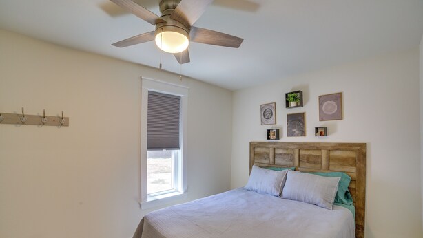 Ein Schlafzimmer mit einem Bett, Deckenventilator, einem Fenster mit Jalousien und Wandbildern.