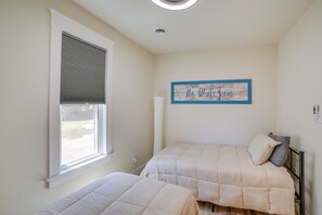Um quarto com duas camas, uma janela com persianas, uma placa na parede e um ventilador de teto.