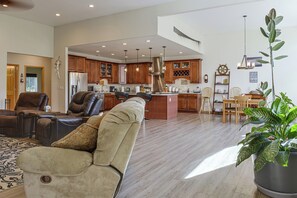 A spacious living room with a leather sofa, a dining area with wooden chairs, and a kitchen with wooden cabinets and stainless steel appliances. - Exquisite Private Home Retreat Near Kenai River (Soldotna)