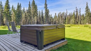 Ein Whirlpool auf einer Holzterrasse mit einer Rasenfläche und Bäumen im Hintergrund.