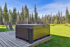 A hot tub on a wooden deck with a grassy area and trees in the background. - Exquisite Private Home Retreat Near Kenai River (Soldotna)