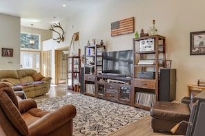 En stue med en brun lædersofa, et mønstret tæppe, et fjernsyn og et træunderholdningsmøbel med diverse genstande.