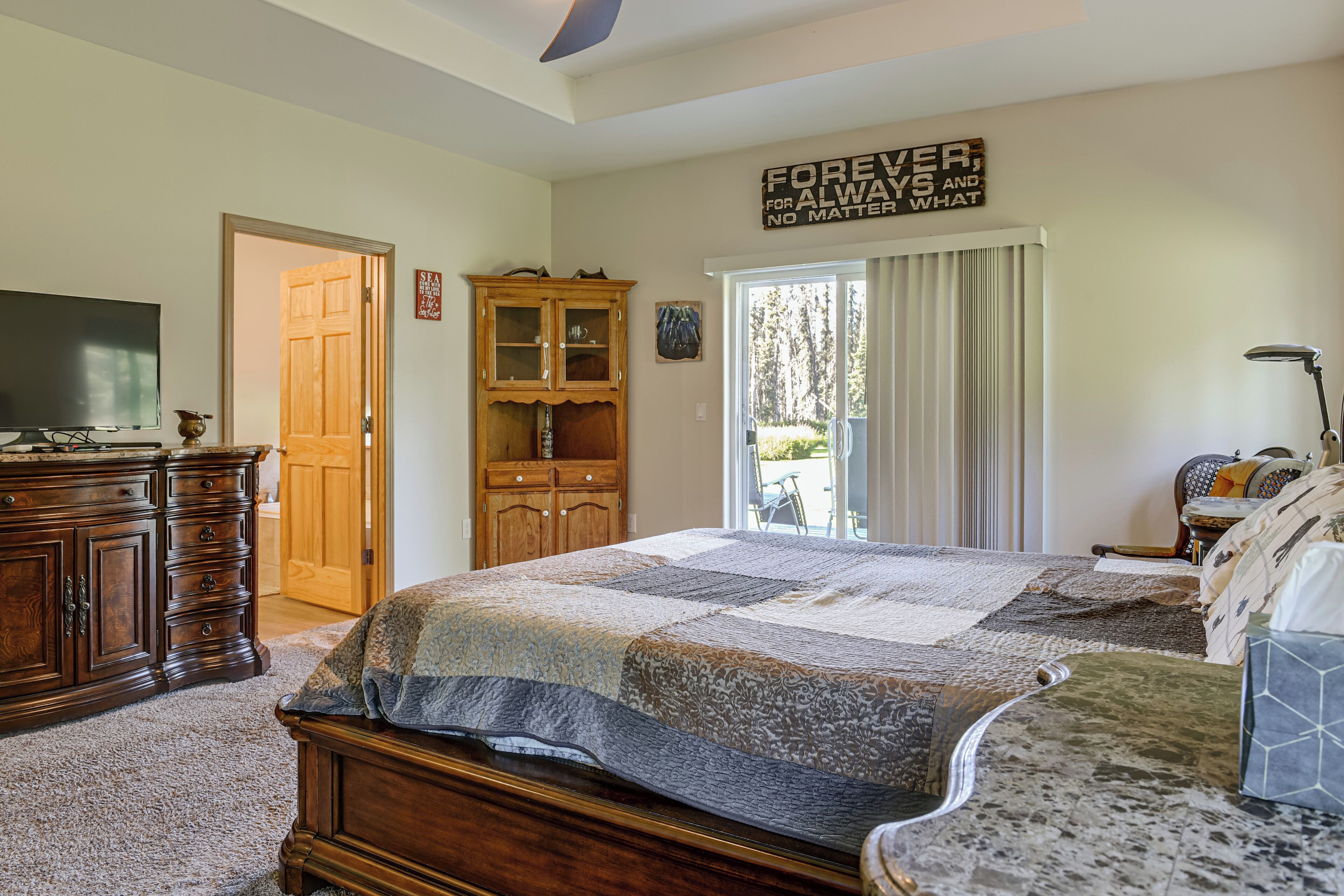 Ein Schlafzimmer mit einem großen Bett, Holzmöbeln, einem Fernseher und Blick ins Freie.