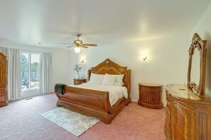 A bedroom with a wooden bed, a ceiling fan, a nightstand, a dresser, a mirror, and a window with curtains. - Backyard Oasis! Spacious Tulsa Home w/ Pool (Tulsa)