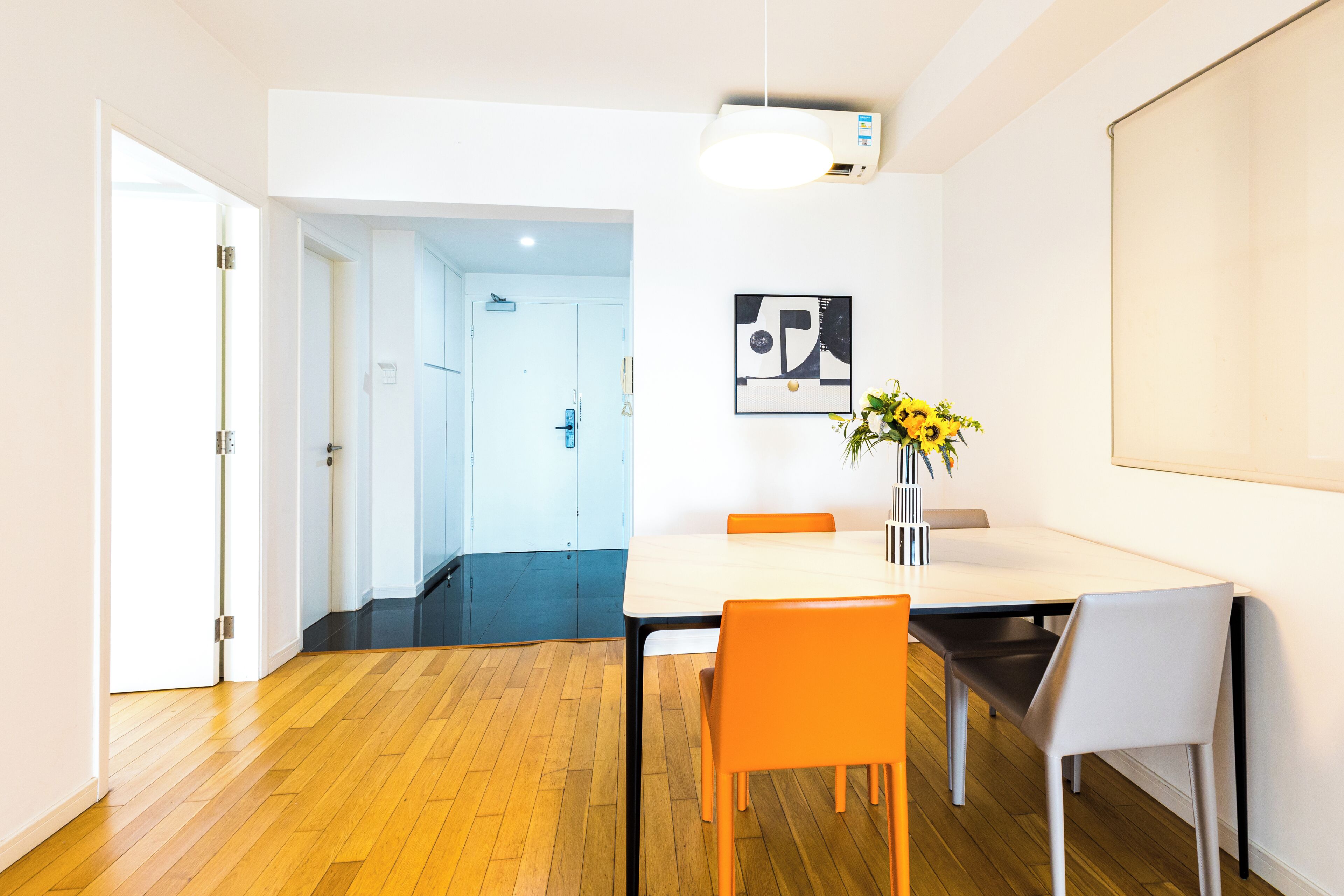 A modern dining area with a wooden floor, a white table, and orange chairs.