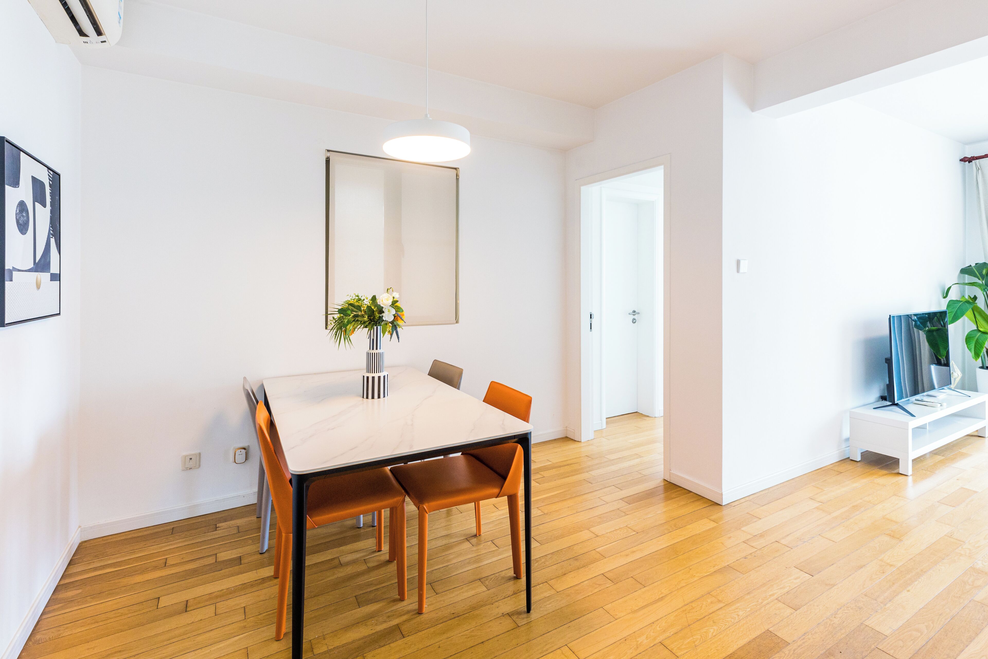 A modern dining area with a wooden table, chairs, and a vase of flowers.