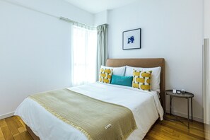 Habitación de hotel con cama, mesita de noche, un cuadro en la pared y una ventana con cortinas.