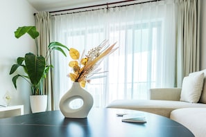 Una habitación con una mesa redonda, un sofá, una planta en maceta y un florero con flores secas.