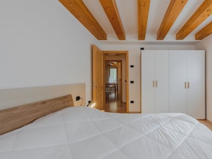 A bedroom with a bed, wooden ceiling beams, a wardrobe, and a door leading to a hallway. - Apartment Rugia by Interhome (Pinzolo)