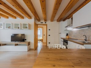 A modern kitchen with wooden beams, white cabinetry, and a dining area with a wooden table and chairs. - Apartment Rugia by Interhome (Pinzolo)