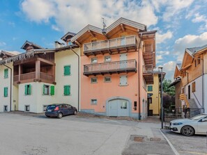 A row of multi-story buildings with balconies, a car parked in front, and a clear sky. - Apartment Rugia by Interhome (Pinzolo)