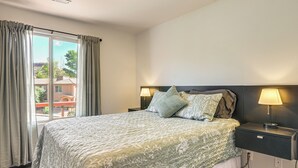 Ein Hotelzimmer mit einem großen Bett, zwei Nachttischlampen, einem Fenster mit Vorhängen und Blick auf Gebäude.