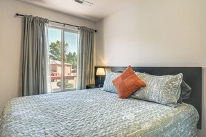 A hotel room with a large bed, a nightstand, a lamp, and a view of buildings through the window. - Gateway to Zion! Retreat w/ Pool & Hot Tub Access (Kanab)
