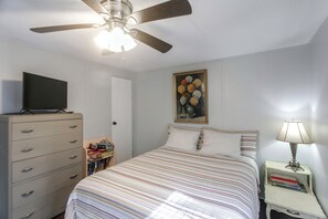 Une chambre à coucher comprenant un lit, une commode, un téléviseur, un ventilateur de plafond, un tableau et une lampe de chevet.