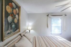 A bedroom with a bed, a painting, a lamp, and a window with curtains.