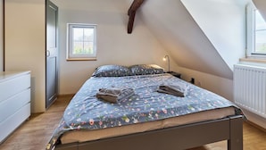 Quarto com teto inclinado, cama com roupa de cama florida, mesa de cabeceira e uma janela.