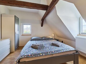 Ein Schlafzimmer mit schrägen Wänden, einem Bett mit Blumenmuster auf der Bettwäsche, einem Nachttisch und einem Fenster.