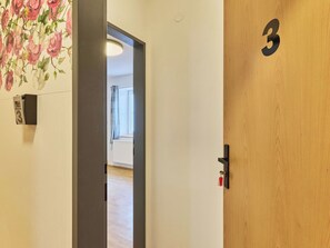 Ett hotellrum med en trädörr märkt med nummer 3, en telefon som sitter fast på väggen och en blommig tapet.