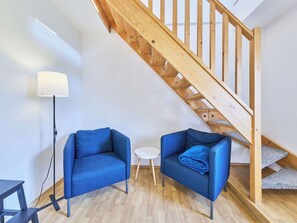 Ein moderner Raum mit einer Holztreppe, zwei blauen Sesseln, einem kleinen weißen Tisch und einer Stehlampe.