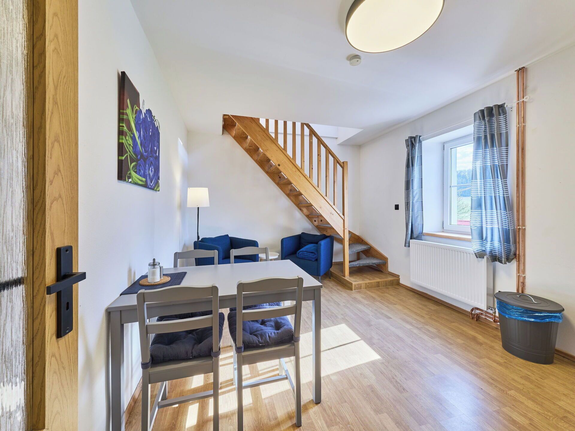 A modern living space with a dining area, a staircase, and a view of the outdoors.