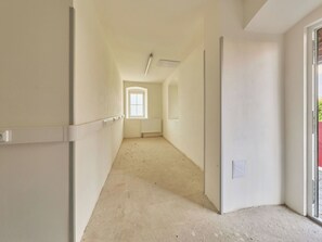 Ein schmaler Korridor mit schräg verlaufender Decke, einem Heizkörper und einem Fenster am Ende.