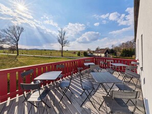 Eine Terrasse im Freien mit Tischen und Stühlen, einem roten Geländer und Blick auf die Landschaft.
