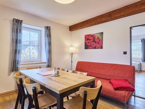 Ein Zimmer mit einem Holztisch, vier Stühlen, einem roten Sofa und einem Gemälde mit roten Rosen an der Wand.