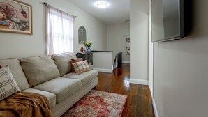 A living room with a sofa, a flat-screen TV, a dining area with a table and chairs, and a hallway leading to another room. - Walk to Water, Dining! Modern City Point Haven (New Haven)