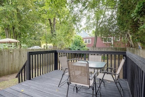 Eine Holzterrasse mit Tisch und Stühlen, umgeben von einem Holzzaun und Bäumen.