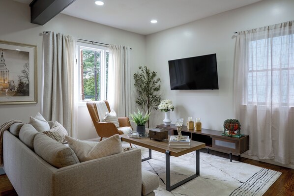 A living room with a sofa, armchair, coffee table, and a flat-screen TV mounted on the wall.