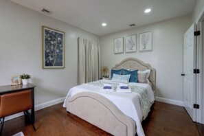 A bedroom with a bed, a desk, and a chair. There are wall-mounted air vents and a door.
