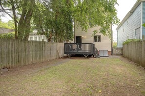 A fenced backyard with a wooden deck, a house in the background, and a clear sky.
