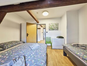 Ein Schlafzimmer mit zwei Betten, einem grünen Sessel, einer weißen Kommode und einem Bild an der Wand.