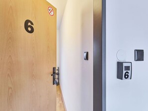 Puinen ovi, jossa on numero 6, tupakointikieltokyltti, avainkortin pidike ja ovikello.