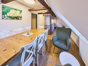 Ein Essbereich mit einem Holztisch, weißen Stühlen und einem grünen Sessel.